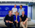 Group photo of five MEPs from Volt Europa at the European Parliament. They are seated on a light-colored couch in front of a blue wall with the European Parliament logo and multilingual text that reads “European Parliament.” From left to right: seated in front are Damian, Anna, and Kai, while Reinier and Nela stand in the back, all smiling. The setting is modern and well-lit.